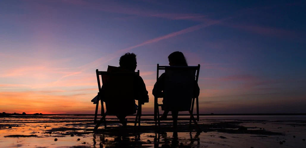 A couple sits in their Cape Cod Beach Chairs enjoying a beautiful sunset on the bay